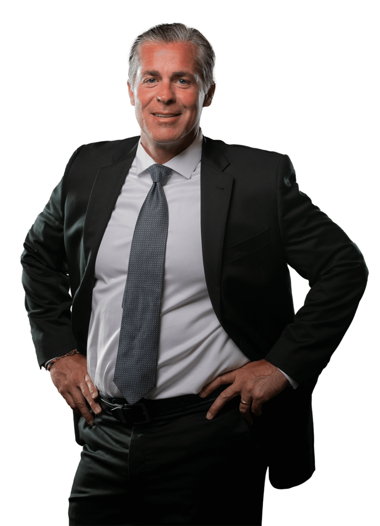 Dan Giroux smiling with his hands on his hips. He is wearing a black suit with a dark gray tie.