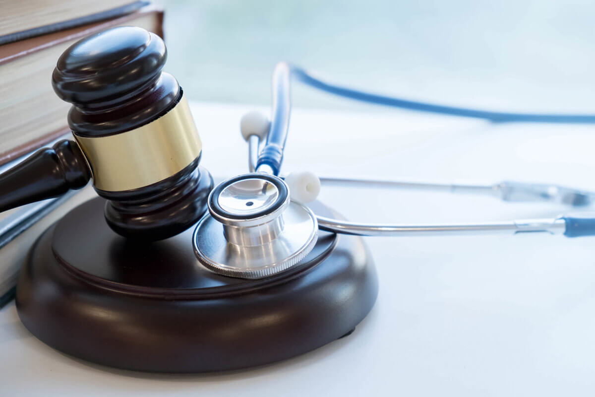 A gavel and stethoscope sit on a table with a book in the background.