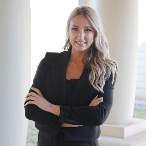 Kassidy Watkins stands smiling in a black suit.