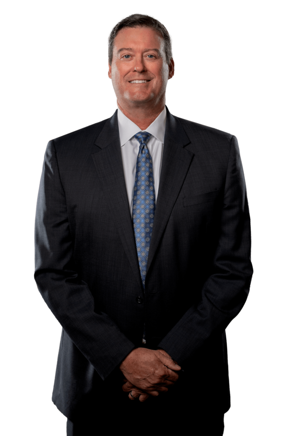 Paul Dugan Jr. standing in a dark gray suit with a blue tie. He is smiling.